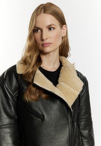 Giacca in pelle nera con colletto in shearling beige, dettagli con zip e finitura testurizzata, caratterizzata da una vestibilità comoda e un design robusto.
