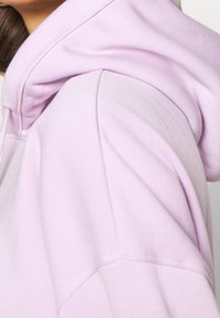 Felpa con cappuccio di un morbido colore viola chiaro, con una consistenza soffice, cappuccio arrotondato e cuciture visibili sulle spalle e sulle maniche.