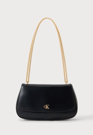 Sac bandoulière en cuir noir avec bandoulière chaîne dorée et petit logo doré cK sur le rabat avant, posé sur un fond blanc uni.