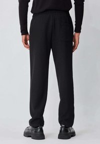 Pantalon noir en tissu léger avec une ceinture élastique. Il présente une poche arrière et une coupe droite. Assorti à des chaussures noires.