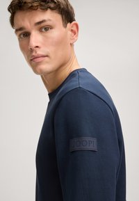 Navy blue long-sleeve t-shirt made of soft cotton, featuring a round neckline and a rubberized JOOP! logo patch on the left sleeve.