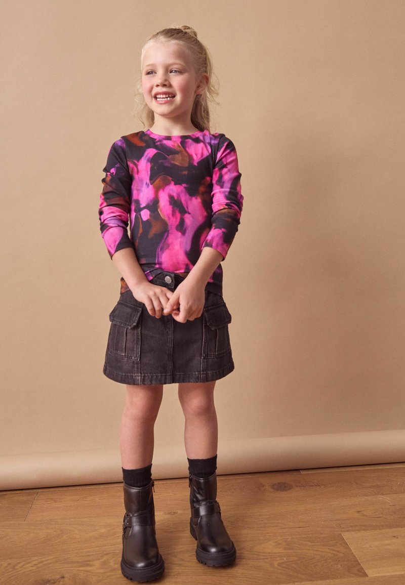 Langermige top met een zwart, roze en bruine abstracte print; donkere spijkerrok met zakken; zwarte enkellaarsjes met gespdetail.