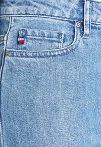 Ljust blå denimjeans har en liten röd, vit och blå logotagg på framfickan. Texturen är något urtvättad med synliga sömdetaljer.
