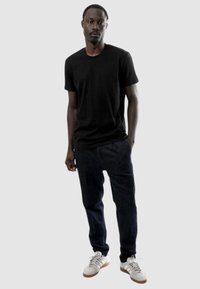 T-shirt nera a maniche corte, vestibilità rilassata, abbinata a jeans scuri e sneakers bianche con suola color sabbia. Design semplice e casual senza fantasie.