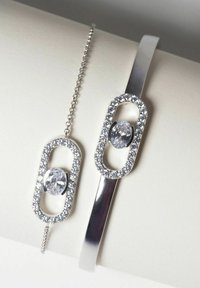 Bracciale in argento e bracciale a catena, entrambi con pietre ovali trasparenti circondate da accenti scintillanti, superfici lisce e forme geometriche moderne.