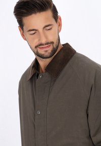 Olijfgroene jas met een bruine corduroy kraag, voorzien van een drukknoopsluiting, lichtgewicht stof en een soepele textuur.