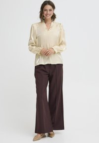 Satin elfenbenbluse med flæser ved halsudskæringen og lange pufærmer, parret med brede bordeaux bukser. Beigemuler afslutter outfittet.