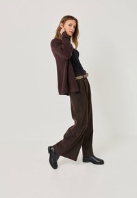 Brown fuzzy cardigan, black top, brown wide-leg trousers, and black shoes with textured detailing. Outfit with a leopard print belt.