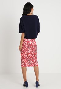 Mörkblå kortärmad stickad topp i kombination med en kroppsnära, blommönstrad röd midikjol, bärs med blå klackskor med blockklack.