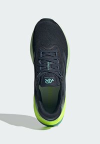 Černá a zelená sportovní bota s síťovaným svrškem, zaoblenou špičkou a silnou podrážkou. Mezi detaily patří logo a vzorované boční ozdoby.