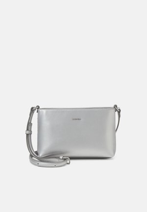 Sac bandoulière en cuir argenté avec une texture lisse, fermeture éclair et sangle réglable. Présente un logo sobre à l'avant.