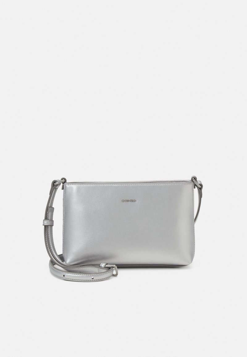 Srebrna torebka typu crossbody ze skóry z gładką teksturą, zamknięciem na zamek i regulowanym paskiem. Posiada subtelne logo z przodu.