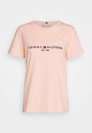 Peach-colored cotton t-shirt with short sleeves. Features "TOMMY HILFIGER EST. 1985" logo in navy with a red and white emblem.