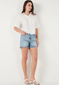 White button-up shirt with short sleeves, paired with light blue denim shorts. Silver sandals complete the outfit.