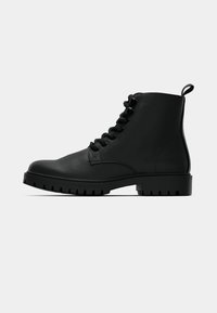 Botină din piele neagră cu șireturi, la gleznă, cu talpă durabilă și cu un tab la spate, prezentată din lateral pe un fundal alb.