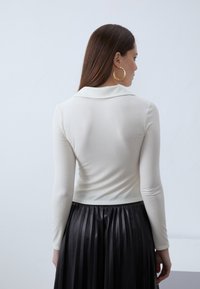 Fitted cream long-sleeve top with a collared neckline, paired with a pleated black skirt. The top features a ribbed texture.