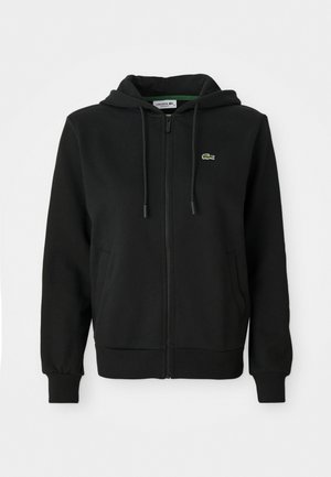 Schwarzer Reißverschluss-Hoodie aus weichem Stoff. Mit einer Kapuze mit Kordelzug, gerippten Bündchen, Seitentaschen und einem kleinen grünen Logo auf der Brust.