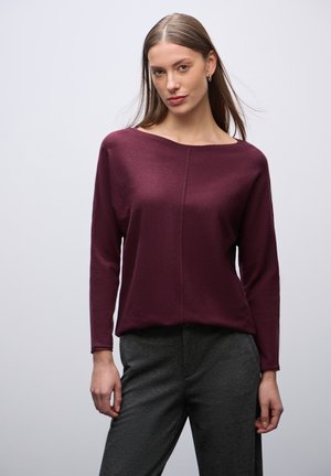 Burgundská halenka s dlouhým rukávem, širokým lodním výstřihem, texturovanou látkou a volným střihem, doplněná tmavě šedými kalhotami.