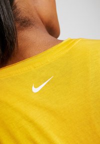 Camiseta de algodón amarilla con cuello redondo y un logo de Nike blanco en la parte posterior del cuello, mostrando una textura suave y un diseño simple.