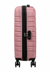 Valigia rigida rosa con superficie texture, zip nera, lucchetto a combinazione integrato e quattro ruote per la mobilità.