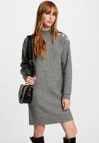 Abito in maglia a coste grigia con collo alto, maniche lunghe e bottoni decorativi su una spalla. Texture morbida e design di lunghezza media.