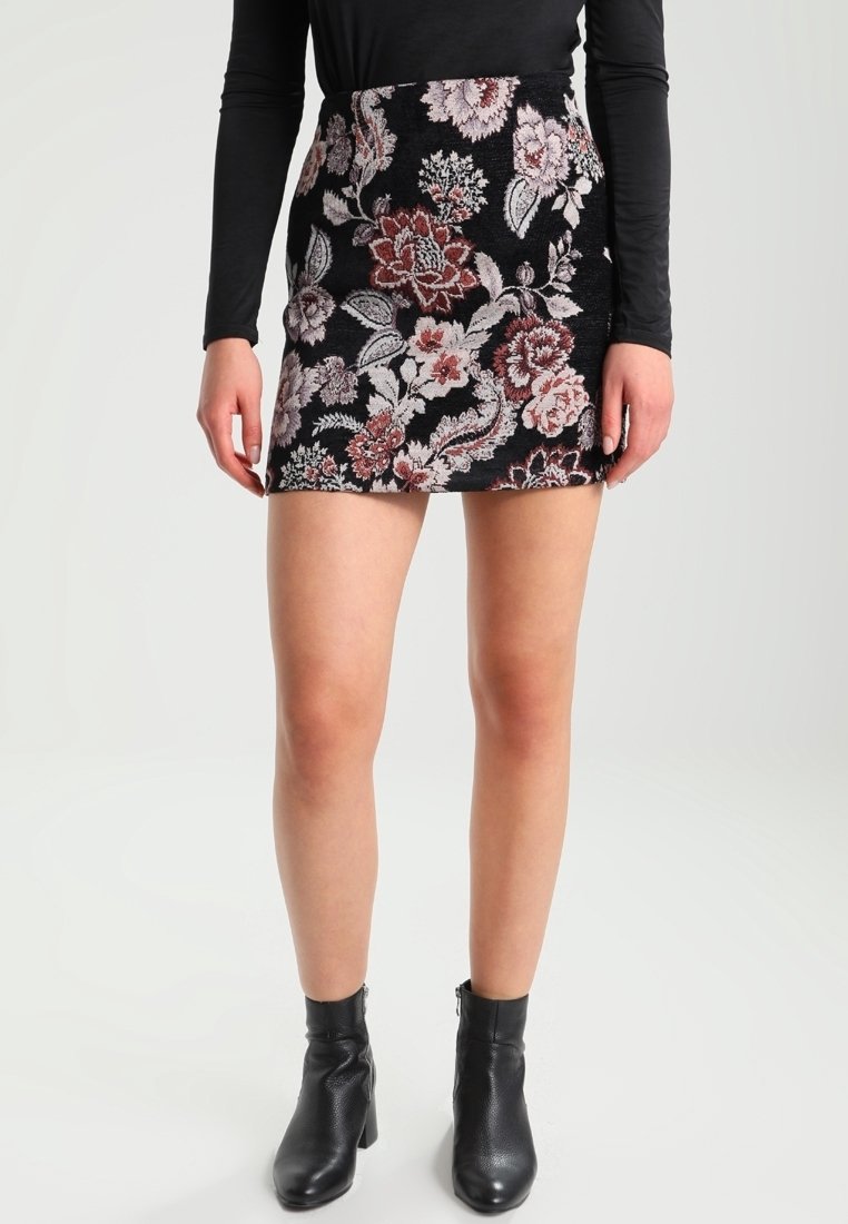 Jupe mini noire à motifs floraux présentant des motifs complexes en rose et blanc. Portée avec un haut fitted à manches longues noir et des bottines.