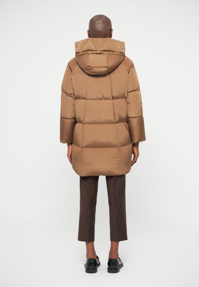 Hnedý puffrový kabát s kapucňou, s prešívanými štvrcami a širokými rukávmi, nosený nad hnedými nohavicami a čiernymi topánkami.