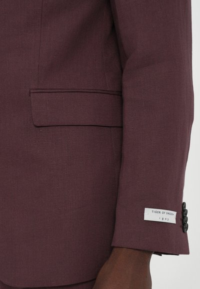 Weinroter Blazer aus strukturiertem Stoff, ausgestattet mit einer Brusttasche, einem Vier-Knopf-Manschettenverschluss und einem Markenlabel am Ärmel.