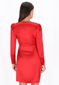 Abito rosso in satin con maniche lunghe, design aderente e lunghezza fino a metà coscia. Presenta spalle a sbuffo e una vita sartoriale.