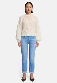 Maglione crema a trecce con dettaglio a rete sul collo, abbinato a jeans blu chiaro e ballerine marroni con stampa leopardata.