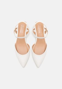 White vegan leather pointy-toed flats with a strap design; smooth texture; tan insoles featuring brand logo; minimalistic style.