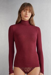 Burgundy dlouhý rukáv rolák vyrobený z texturované, elastické látky. Má přiléhavý siluetu, měkký límec a jemný lesk.