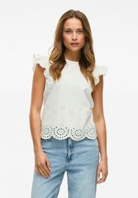 Hvid ærmeløs bluse med volanter på skuldrene, dekoreret med broderet blomster motiver langs kanten og bølget kant.