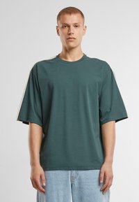 Rövid zöld, oversized pamut póló, kontrasztos krém csíkozással a vállrészen és klasszikus környakú fazonnal.