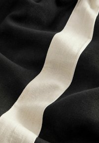Zwarte stof met een crèmekleurige golvende streep. De textuur komt zacht en lichtjes getextureerd over, wat de contrast tussen de kleuren benadrukt.