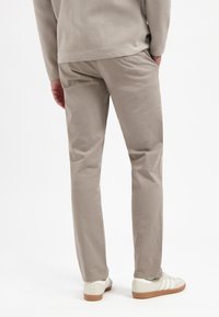 Beige chino's met een gladde textuur, rechte snit en achterzakken, gedragen met witte sneakers en een grijze lange mouwen top.