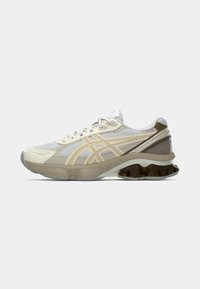 Lightweight running shoe with a mesh upper in gray and beige, accented with yellow stripes. Features a cushioned sole with a unique design.