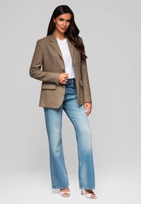 Hnědý strukturovaný blazer přes bílý tričko, spárovaný se světle modrými zvonovými džíny a bílými sandály na podpatku. Proporcovaný střih s dvěma kapsami.