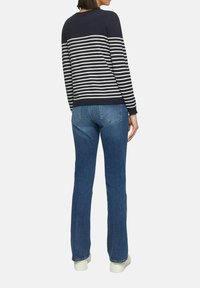 Marineblau gestreifter Pullover mit cremefarbenen horizontalen Streifen, kombiniert mit blauen Schlagjeans und weißen Sneakern, zeigt ein lässiges Outfit.