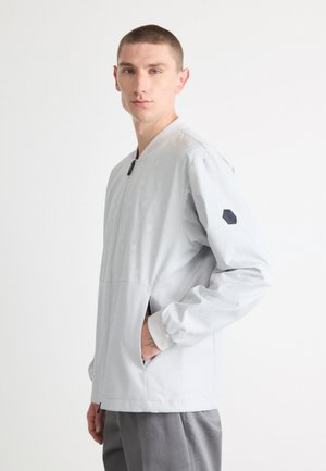 Chaqueta de pullover gris claro con un sutil patrón hexagonal, que presenta un cuello alto, bolsillos laterales y un acento en forma de hexágono en los hombros en color negro.