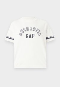 Bílý tričko s krátkým rukávem s potiskem "AUTHENTIC GAP" v námořnické modři, s pruhovanými akcenty na rukávech. Vyrobeno z měkké bavlny.