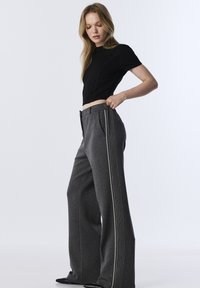 Černý krátký top s krátkými rukávy, který je doplněn o šedé kalhoty s širokým střihem a svislými bílými pruhy a bočními kapsami. Hladká textura látky.