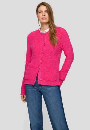 Weicher rosa Cardigan mit langen Ärmeln, Taschen vorne und Knöpfen. Getragen über einem weißen Hemd mit Kragen, kombiniert mit blauen Jeans.