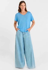 Light blue short-sleeve top with a V-neck and loose-fitting, high-waisted wide-leg light denim jeans, featuring front pockets.