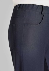 Marineblaue Hose aus strukturiertem Stoff, mit elastischem Bund und einer Seitentasche. Das Design umfasst sichtbare Nähte und einen maßgeschneiderten Schnitt.