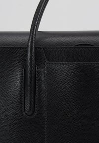 Svart läderhandväska med en strukturerad yta, släta handtag och en vass form. Noterbara detaljer inkluderar en framficka och en minimalistisk design.