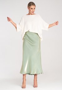 Weißes, übergroßes Strickoberteil mit weiten Ärmeln und einem drapierten Saum, kombiniert mit einem satinierten Sliprock in mintgrün, der eine sanfte Silhouette schafft.