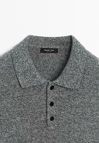 Szara dzianinowa koszulka polo z kołnierzykiem, z teksturowanym wzorem i trzema czarnymi guzikami. Wewnątrz kołnierzyka widoczna metka marki.