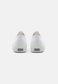 Hvite kanvas sneakers med en teksturert gummisåle og detalj med svart logo på hælen. Rundt tå og kontrastfarget tekstilfôr ved åpningen.
