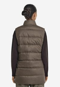 Brun pufferväst med hög krage och vadderad design, med en slät yta och ärmlös snitt. Diskreta detaljer i materialet.